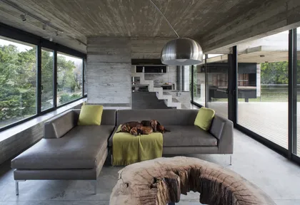 Living moderno con sofá gris, grandes ventanales y techo hormigón visto — proyecto Casa Cariló, por Luciano Kruk, en Cariló
