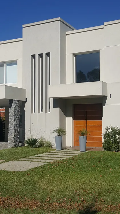 Fachada moderna con puerta de madera y jardín — proyecto EL CARDAL DE LOS CARDALES L45, por LESSI ARQUITECTURA, en Los Cardales