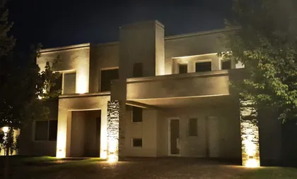 Fachada de casa moderna con iluminación nocturna y detalles en piedra — proyecto LA RESERVA CARDALES - LRCC 195, por LESSI ARQUITECTURA, en Los Cardales
