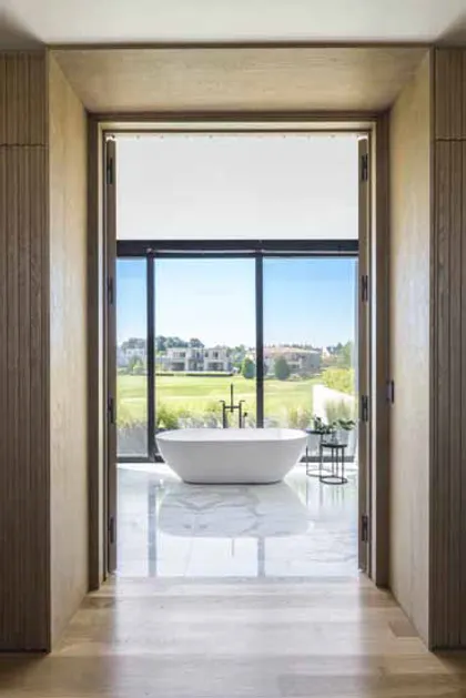 Baño moderno con bañera exenta y vistas panorámicas a campo de golf — proyecto Pilará, por Martin Gomez, en Pilará