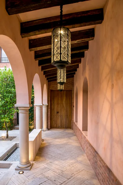 Galería colonial con vigas oscuras, linternas geométricas, arcadas y puerta de madera — proyecto CasaLA, por Ricardo Pereyra Iraola