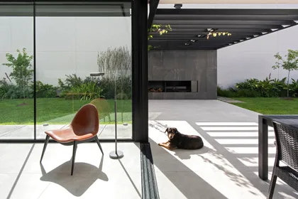 Patio moderno con sillones negros y perro bajo pérgola — proyecto CASA SD28, por GMARQ, en Buenos Aires