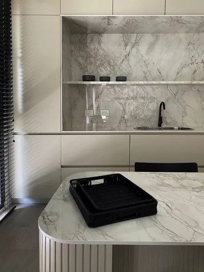 Cocina moderna con paredes de mármol, encimeras y mobiliario beige — proyecto Pampa, por ABEJA CONCEPT, en Belgrano