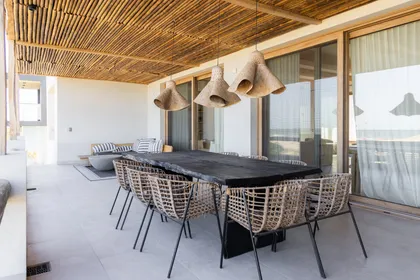 Comedor exterior con techo de madera y muebles de ratán — proyecto El Refugio, por Grupo Pauta Arquitectura, en Pinamar