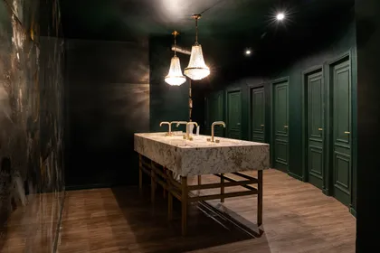 Baño de hotel con paredes revestidas, doble bacha de mármol y luces colgantes — proyecto PRESIDENTE BAR HIPODROMO, por AB ARQUITECTURA, en San Isidro