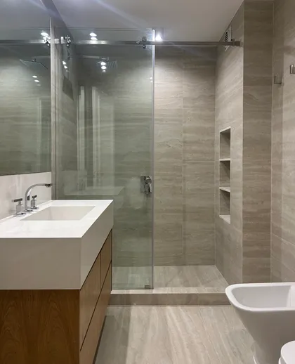Baño moderno con paredes de piedra, vanitory flotante y ducha de vidrio — proyecto QUINTANA, por ESTUDIO TEZ, en Recoleta