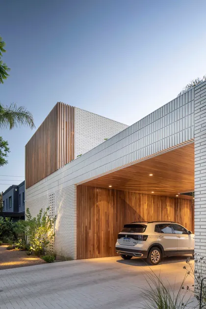 Fachada moderna con ladrillo blanco y madera, cochera integrada — proyecto Casa Magnolia, por Estudio PK, en San Isidro