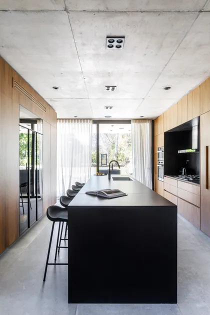Cocina moderna con isla negra, techo de hormigón y paneles de madera — proyecto CASA AH, por GMARQ, en Garin