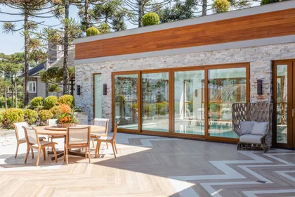 Terraza exterior con mesa de comedor y fachada de piedra y madera — proyecto Projeto Destaque Club&Casa, por OKA ARQUITETURA