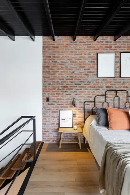 Dormitorio industrial con pared de ladrillo expuesto y escalera flotante — proyecto JURAMENTO, por Nima Estudio, en Buenos Aires
