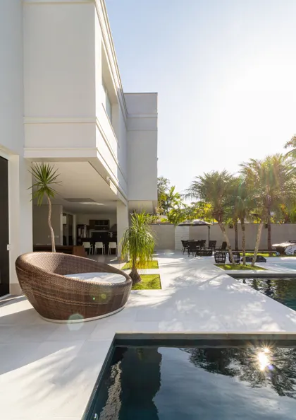 Quincho moderno con piscina, sillón curvo de mimbre y vegetación exuberante — proyecto Mansão de Gabigol, por Carlos Pardal, en Guarujá
