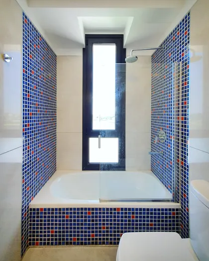 Baño moderno con azulejos azules, bañera blanca y ventana alta — proyecto CASA PUERTOS, por ABAD GADANO, en Belén de Escobar