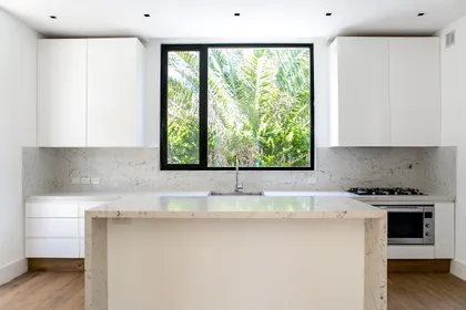 Cocina moderna blanca con isla central y gran ventanal a follaje — proyecto Bosque Chico, por Estudio Arq. María Sioli, en Garin