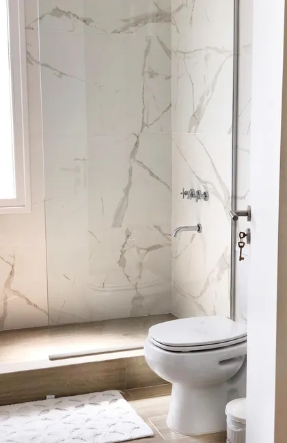 Baño moderno con ducha de mármol, inodoro blanco y luz indirecta — proyecto CASTAÑOS, NORDELTA , por Greschek Obras , en Nordelta