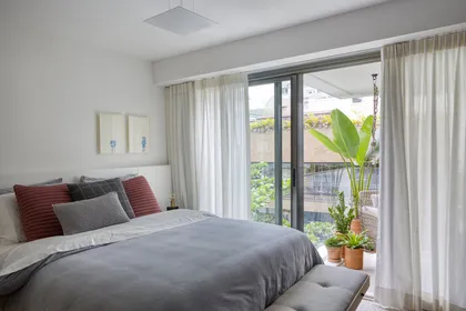 Dormitorio luminoso con cama gris, cortinas y balcón con vista al jardín — proyecto JG House, por Studio Ro-ca
