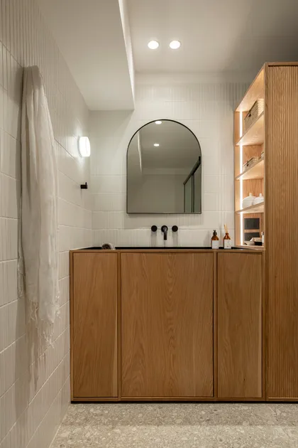 Baño moderno con vanitory flotante de madera y espejo arqueado — proyecto Proyecto Cabello, por Alejandra Nusenovich, en Buenos Aires