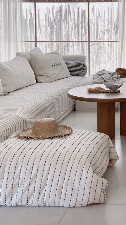 Sala de estar boho con sofá a rayas y otomana de paja — proyecto El Refugio, por Grupo Pauta Arquitectura, en Pinamar