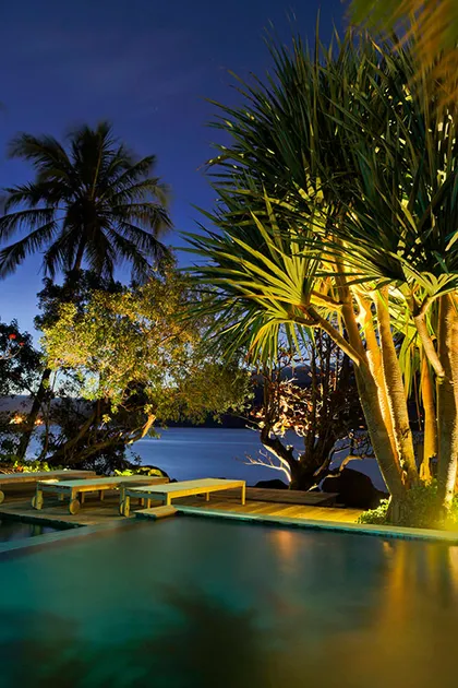 Pileta iluminada al atardecer con deck y palmeras frente al lago — proyecto Arquitetura e Interiores I, por Demian Golovaty