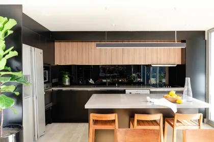 Cocina moderna con isla grande, gabinetes de madera y pared negra — proyecto Guayra - Andrea Gonzales, por ABEJA CONCEPT, en Belgrano