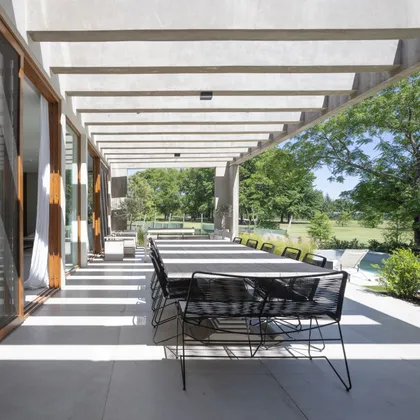 Comedor exterior moderno con pérgola de hormigón y vistas al campo — proyecto CASA BaCa, por Alfredo Orfila arquitectura, en Benavidez