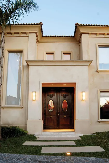 Fachada contemporánea beige con puerta doble de madera oscura iluminada — proyecto Campiña Italiana, por Ciba Arquitectura