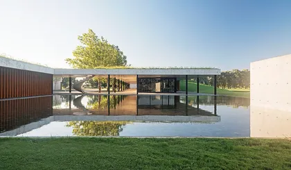 fachada moderna con espejo de agua y vegetación frondosa — proyecto Figueras Polo Stables, por Estudio Ramos, en General Rodríguez