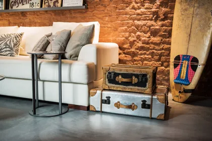Sofá modular beige junto a valijas vintage y tabla de surf — proyecto Defensa, por Estudio Basa, en CABA
