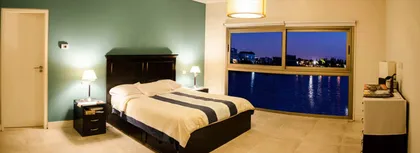 Dormitorio moderno con vista nocturna al lago y pared verde — proyecto Casa Nordelta, por linearecta.arquitectura, en Nordelta
