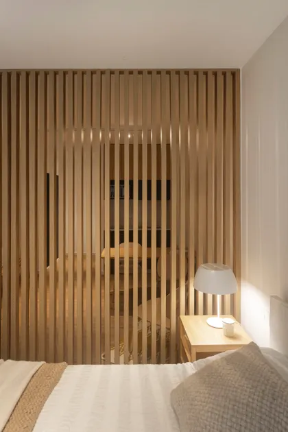Dormitorio moderno con divisor de lamas de madera y cama blanca — proyecto REFORMA NE, por Rastro Estudio, en Palermo