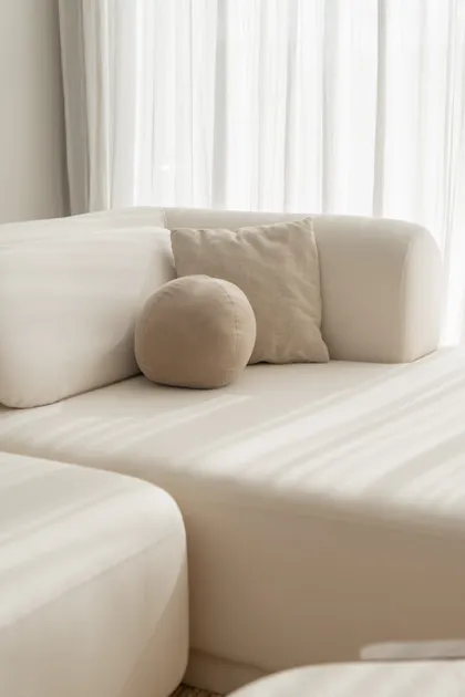Sofá modular curvo beige con almohadones texturizados y cortinas blancas translúcidas — proyecto PROYECTO NAUDIR II, por July Acosta Home, en Belén de Escobar