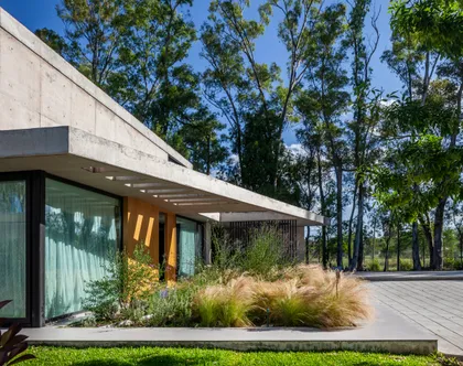 Fachada moderna con concreto y grandes ventanales rodeada de árboles — proyecto Casa ALVA, por V2 Arquitectos, en City Bell