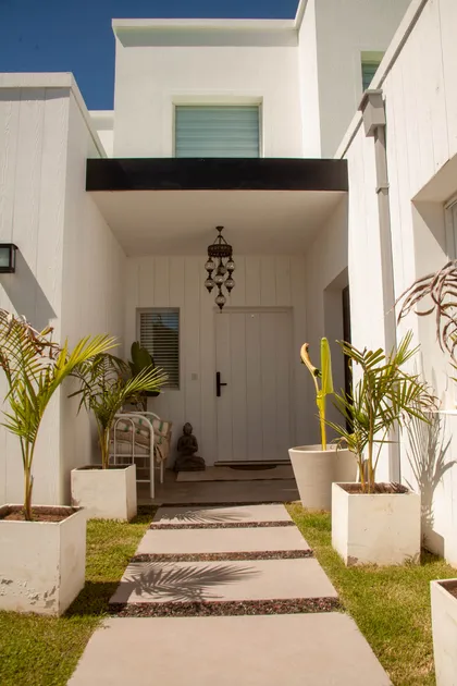 fachada moderna mediterránea con camino de piedra y plantas tropicales — proyecto Obra Fachada Nicole, por Arq. Lourdes Yarade Saravia, en Manzanares