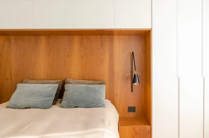 Dormitorio moderno con paneles de madera y luz de pared — proyecto Guayra - Andrea Gonzales, por ABEJA CONCEPT, en Belgrano