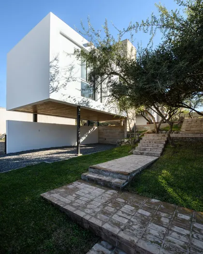 Casa blanca minimalista con jardín, escaleras y pergola de madera — proyecto Casa 3/3, por Momento.