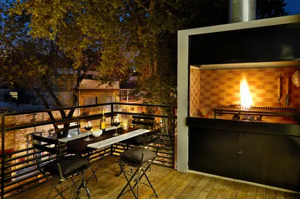 Terraza con parrilla y mesa de comedor al anochecer — proyecto Ravignani Studios II, por Mazzinghi Sanchez, en Palermo