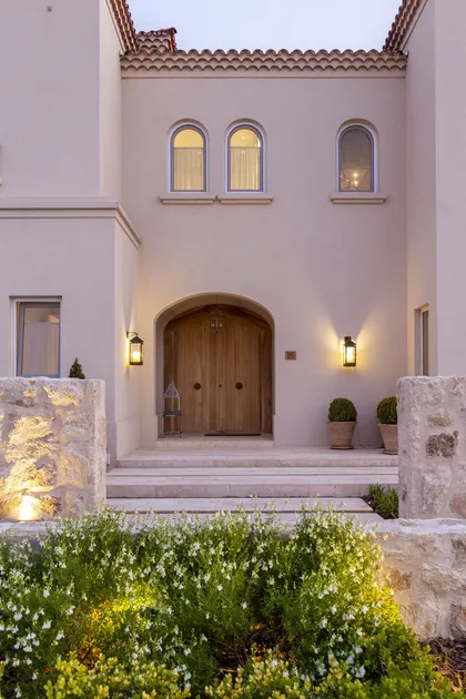 Fachada mediterránea con puerta doble de madera y luces cálidas — proyecto Casa MF, por Estudio Junor, en Belén de Escobar