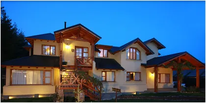 fachada rústica de hotel con madera expuesta y luz cálida — proyecto Apart-Hotel "Posada de Montaña", por ESTUDIO ARQ.GABRIEL ARIAS, en San Carlos de Bariloche