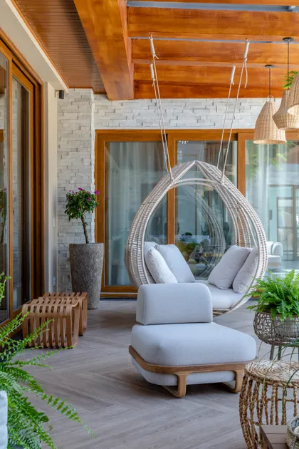Terraza con sillón colgante de mimbre y sillones grises modernos — proyecto Projeto Destaque Club&Casa, por OKA ARQUITETURA