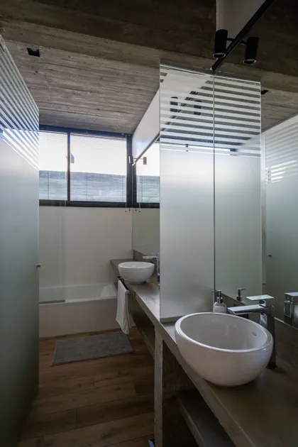 Baño moderno con techo de hormigón, mamparas de vidrio esmerilado y bacha sobre mesada — proyecto Casa Tres Patios, por Besonías Almeida arquitectos, en Pilar