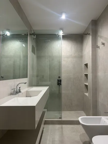Baño moderno con revestimiento de piedra gris y bidet — proyecto QUINTANA, por ESTUDIO TEZ, en Recoleta