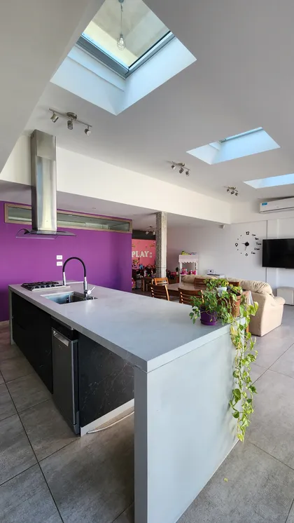 Cocina moderna de concepto abierto con isla de microcemento y pared lila — proyecto Casa Berner, por Zima Arquitectura, en La Plata