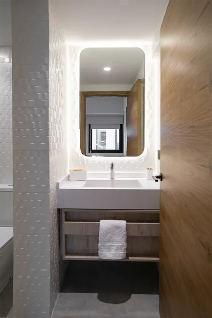 Baño moderno con espejo iluminado, mesada blanca y revestimiento en madera — proyecto Casa Oroño, por Estudio Plats, en Buenos Aires