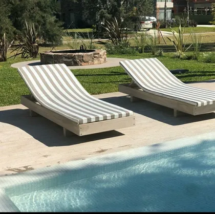 Área de piscina moderna con tumbonas a rayas y fogonero de piedra — proyecto Caning, por Decortinasytelas, en Buenos Aires
