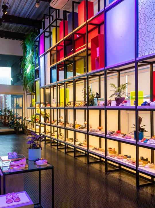 Local comercial con estructura metálica y vitrinas iluminadas en colores neón — proyecto Showroom Melissa, por Pricila Dalzochio