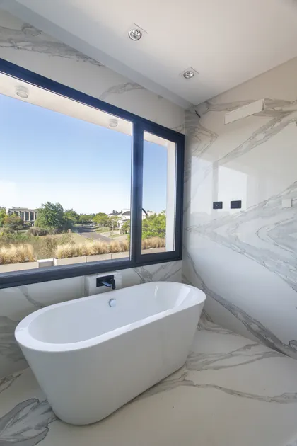 Baño moderno con bañera blanca frente a ventanal con vistas — proyecto El Golf 137 - Nordelta, por Build a Home Arquitectura, en B1624 Tigre