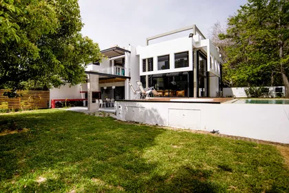 Fachada moderna blanca con grandes ventanales y jardín exuberante — proyecto CASA GONNET, por LEONE LORAY ARQUITECTOS, en Gonnet