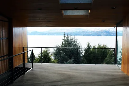 Terraza moderna con vista al lago y revestimiento de madera — proyecto Casa Península San Pedro, por Servente Larrazabal Arq, en Bariloche