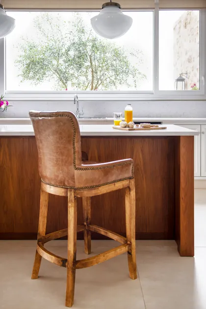 Cocina moderna con isla, ventana amplia y banquetas de cuero — proyecto Casa MF, por Estudio Junor, en Belén de Escobar