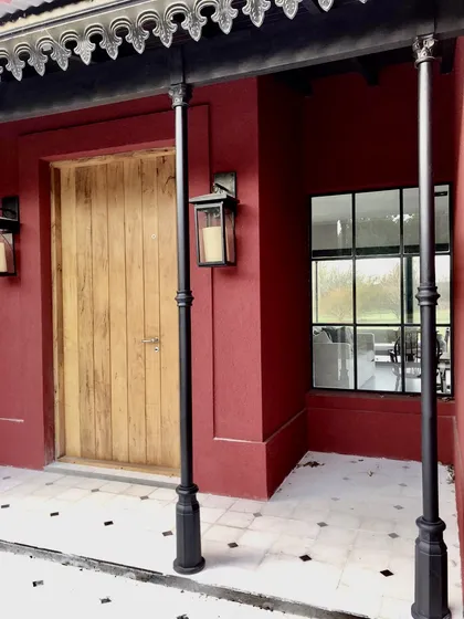 fachada bordo con puerta de madera y pilares negros decorados — proyecto Las Vizcachas, por Marconi Silva Arquitectos, en Los Cardales