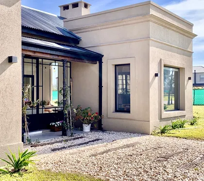 Fachada moderna color beige con grandes ventanales negros y jardín con grava — proyecto Los Jazmines Pilar del Este, por Marconi Silva Arquitectos, en Pilar del Este